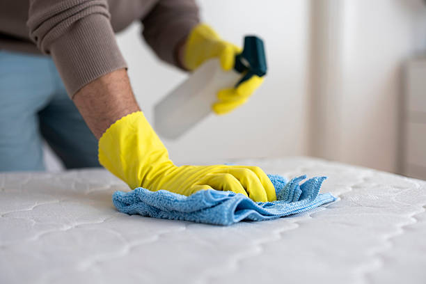 Close-up view of a man cleaning a mattress using a spray bottle and microfiber cloth, representing home hygiene, deep cleaning, and household care.